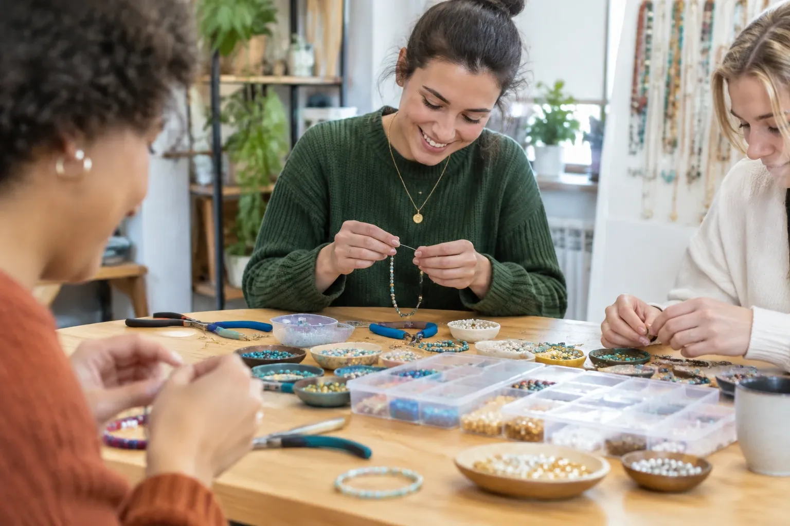 Drie vrouwen aan tafel die kralen en gereedschap gebruiken om armbanden te rijgen
