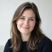 Portret van een vrouw met bruin haar tot op de schouders, donkere trui, lichte effen achtergrond